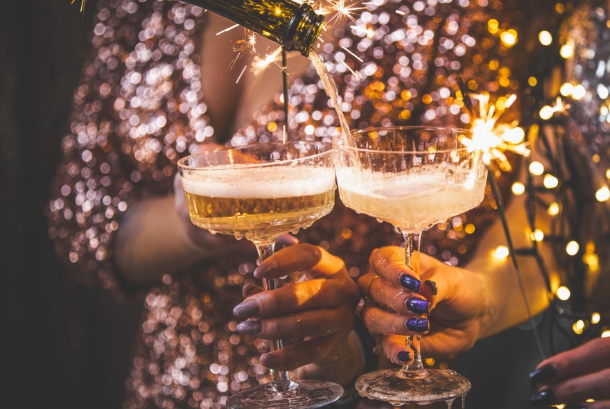 Two hands holding glasses of champagne and sparklers.