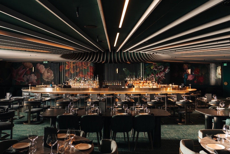 Interior of Amphora restaurant with rows of strip lighting on the ceiling leading to a central bar area, surrounded by dining tables and chairs.
