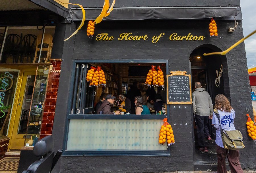 two people are walking into a small restaurant there is a sign saying Heart of Carlton