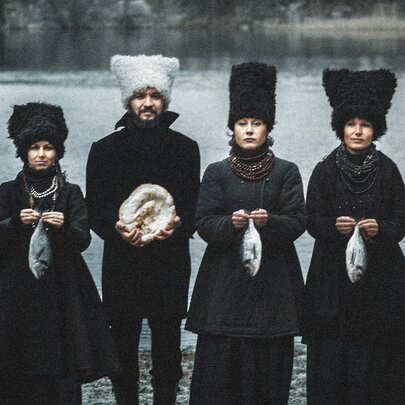 Four members of the group DakhaBrakha in oversized wooly hats and coats beside a lake, each holding a fish.