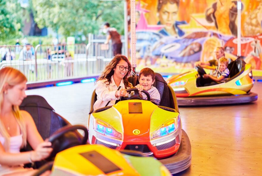 An adult and child inside a dodgem car,steering it around a dodgem track.