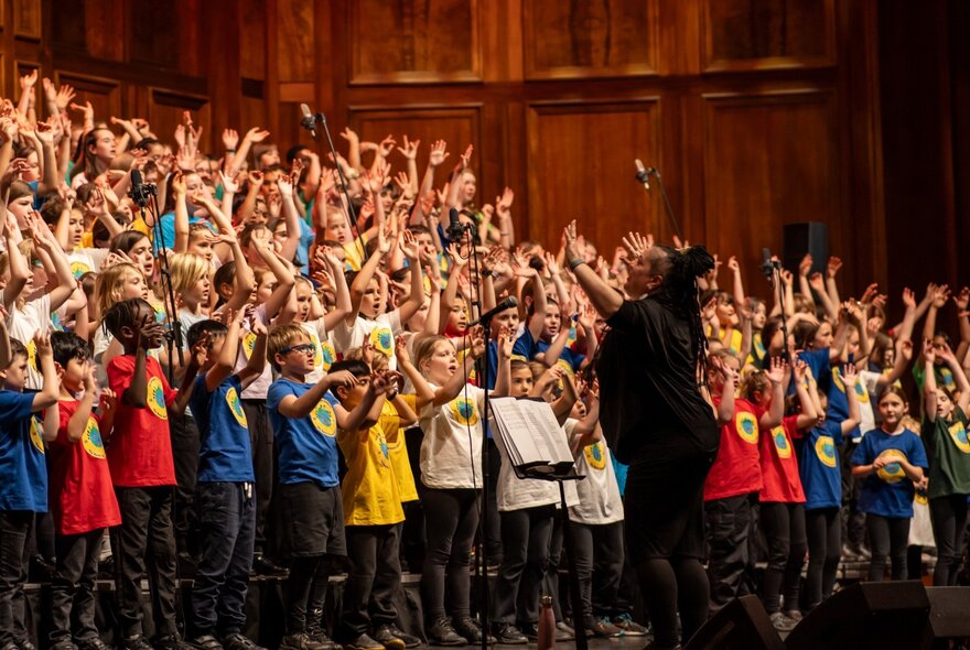 A very large choir of children performing with their hands in the air. 