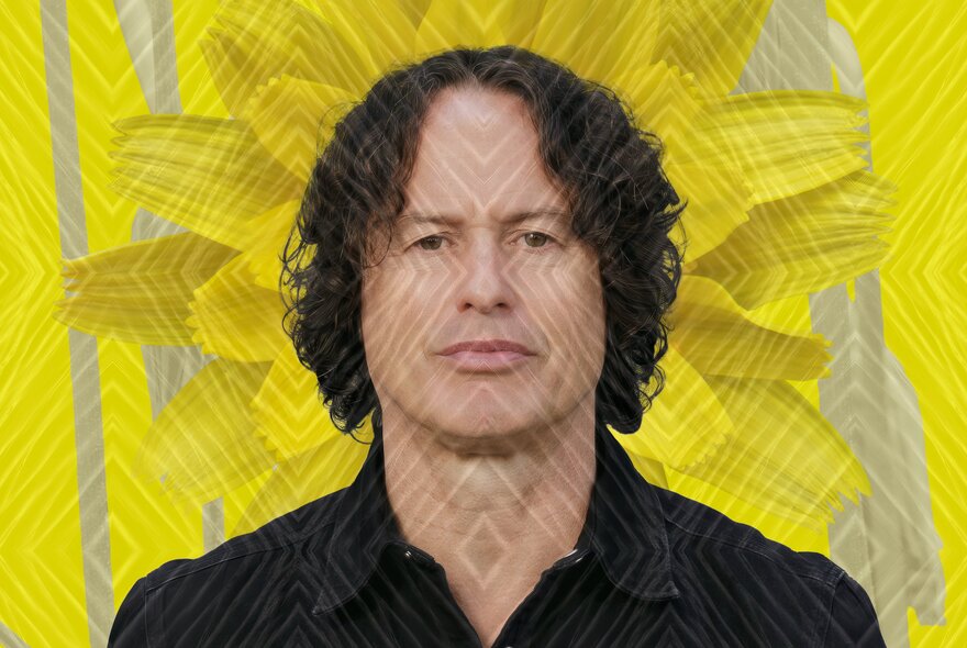 Person with brown hair and a neutral expression looking straight ahead, with a bright yellow flower on a patterned yellow as the background.