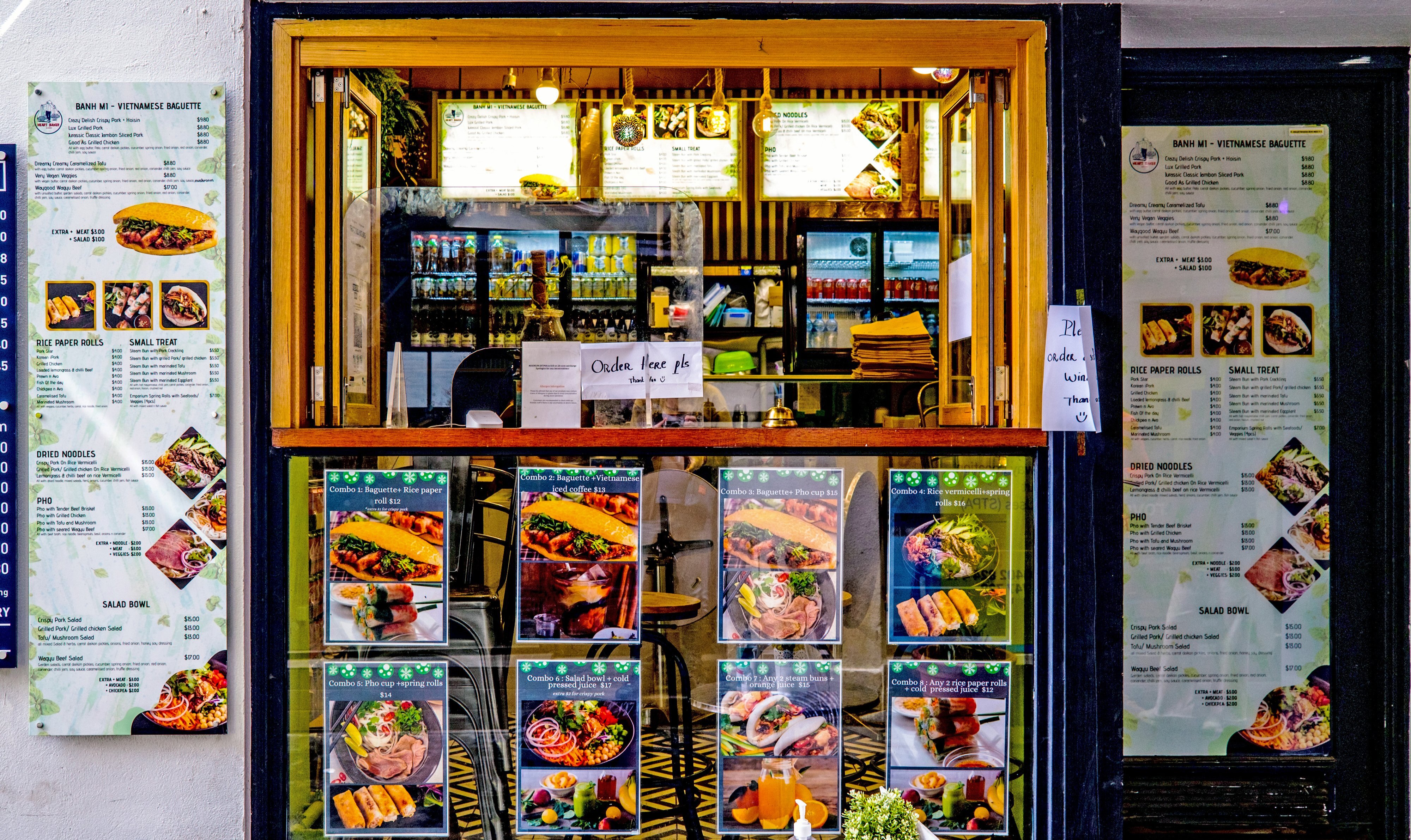 A window shopfront at a Vietnamese banh mi shop with photos of the banh mi on the wall.