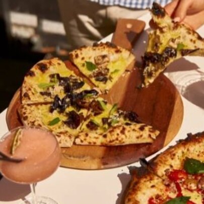 Hands taking slices of pizza from a plate, with drinks.