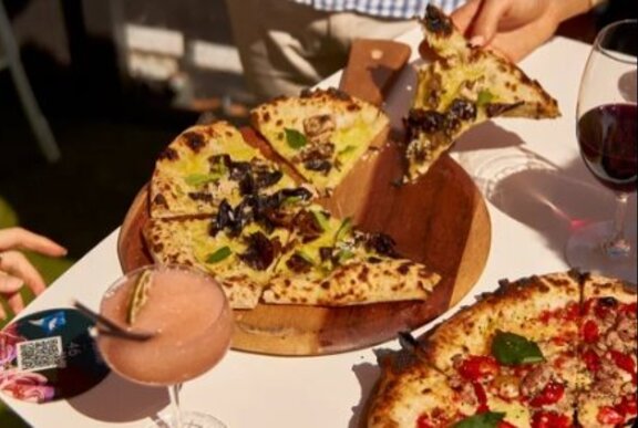 Hands taking slices of pizza from a plate, with drinks.