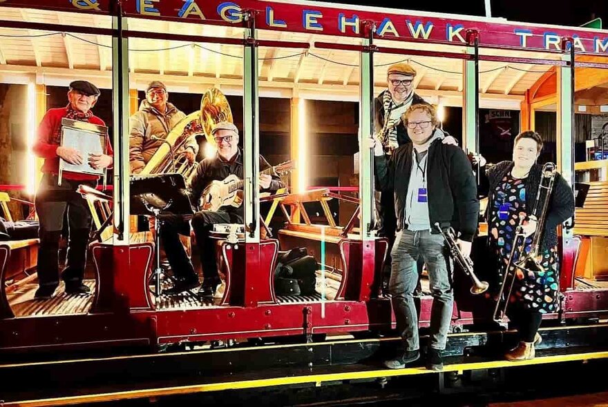 A band of musicians, each holding their instrument, in various positions on a lit-up vintage tram.