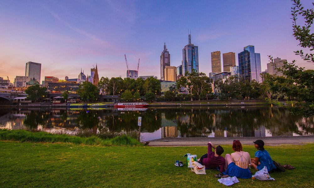 A group of friends sitting beside a city river at sunset.
