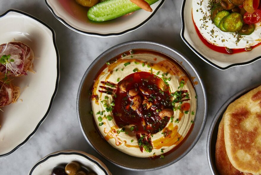 Looking down at a large plate of hummus, and other dishes alongside.