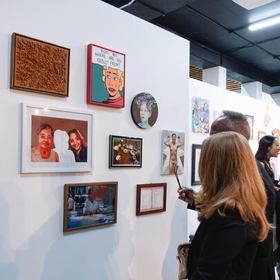 An exhibition of contemporary wall-based artworks in a gallery space, with  people in the space looking at the art.