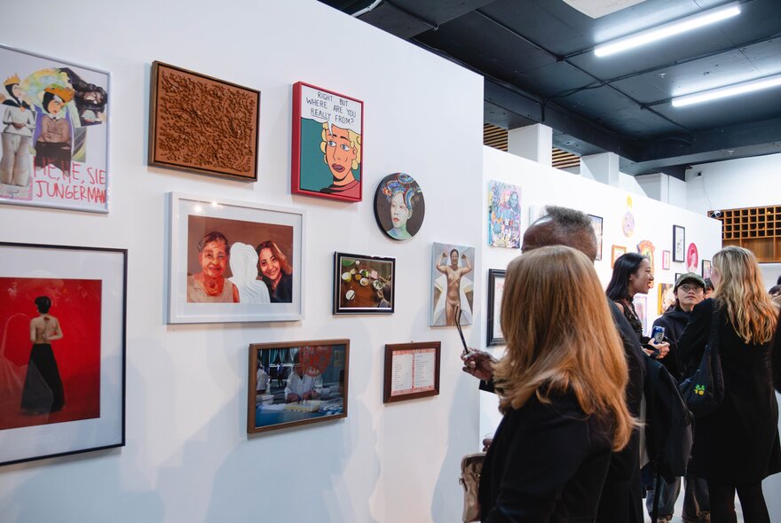 An exhibition of contemporary wall-based artworks in a gallery space, with  people in the space looking at the art.