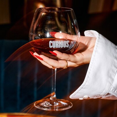 A hand holding up a glass of red wine.