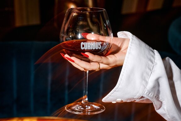 A hand holding up a glass of red wine.