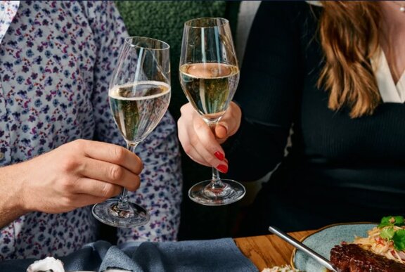 A close up of a couple each holding up a wine glass half-filled with white wine.