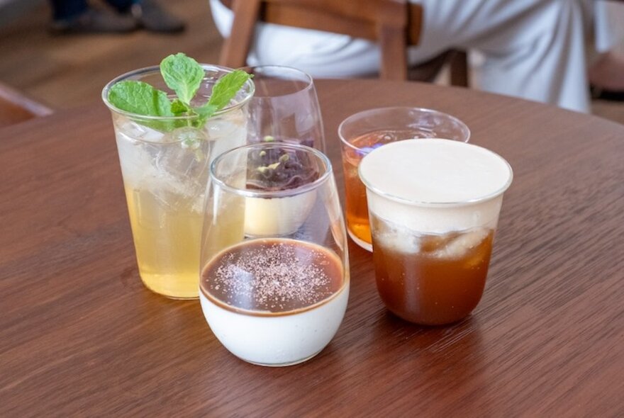 An assortment of coffee, teas and dessert glasses on a wooden table. 