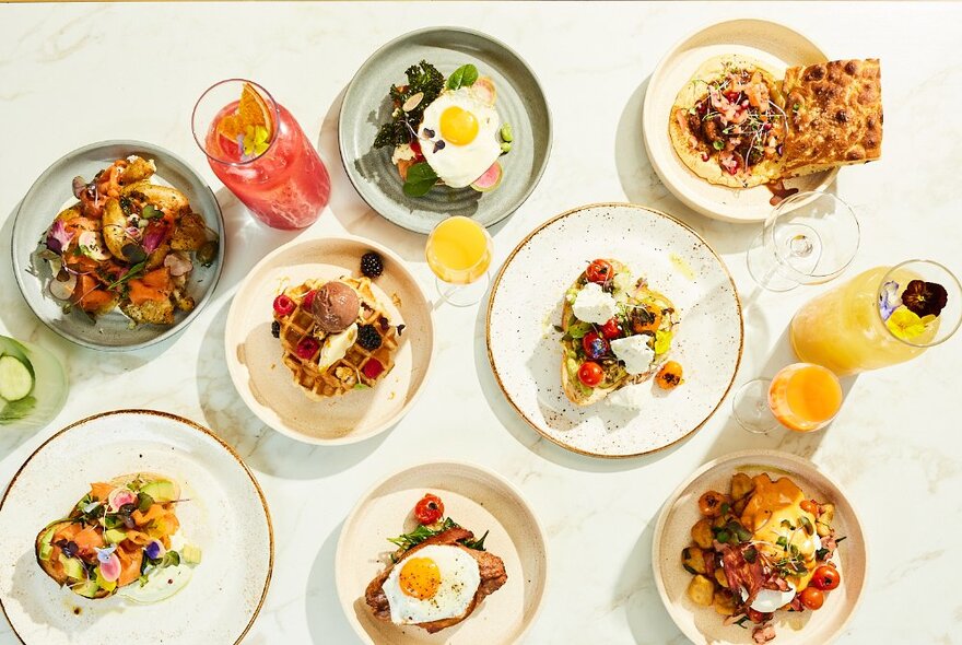 Overhead view of several restaurant dishes including eggs, salads and savouries, with drinks.