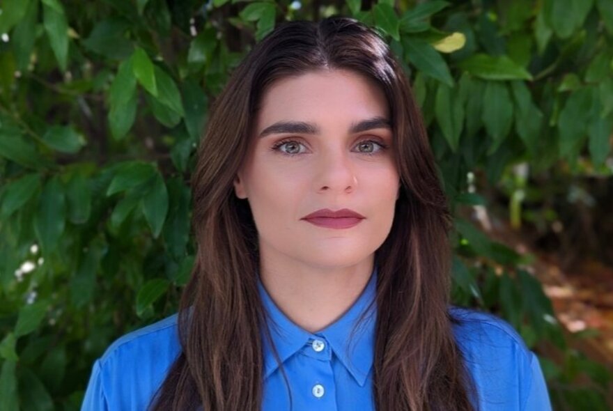 Portrait of Associate Professor Jessica Russ-Smith, wearing a blue shirt and posing in front of a leafy green background.