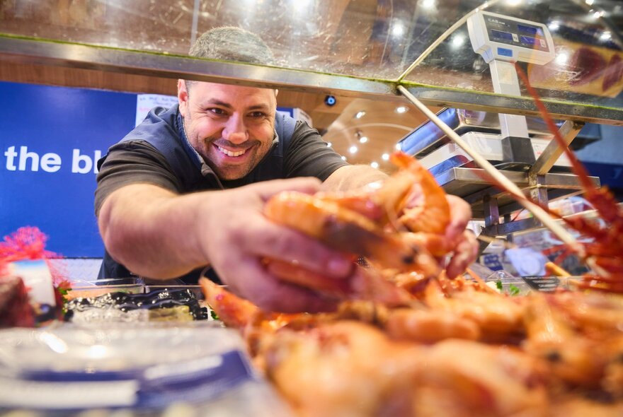 A smiling man grabbing handfuls of cooked prawns. 