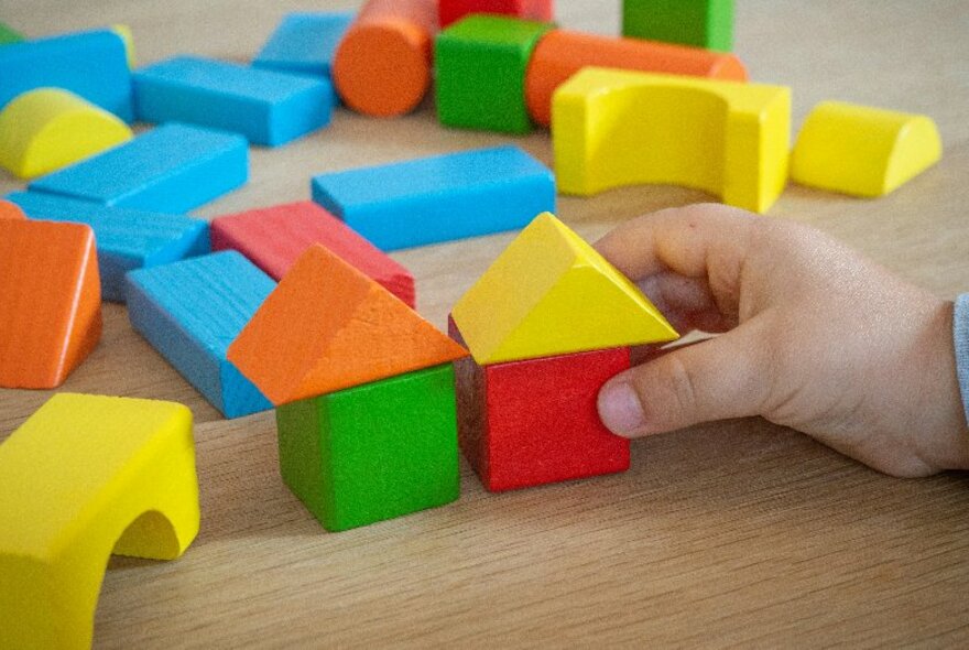 A hand playing with children's coloured wooden building blocks on a flat surface.