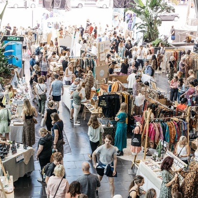Aerial view of an interior market with stalls selling clothing and raft, and many people walking around and shopping in the space.
