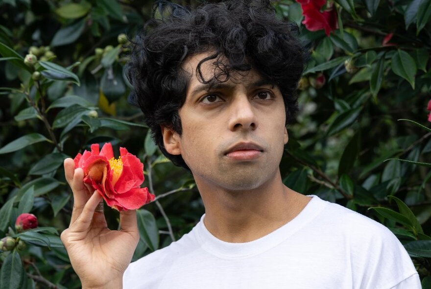 Comedian Rao Morusupalli looking thoughtful in a garden while holding a red camellia.