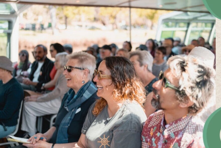 A seated audience listening to a speak who is out of sight.