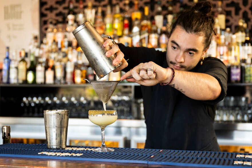 A bartender straining the contents of a cocktail shaker into a glass.