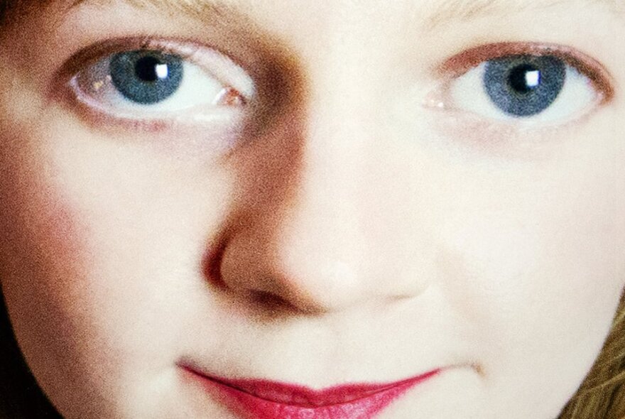 An extreme close-up of a woman's face with doll-like features - big blue eyes and red lips. 