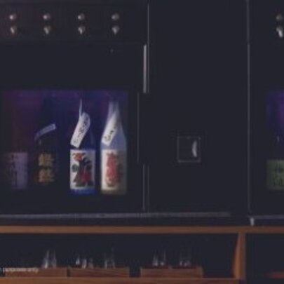 A sake dispenser with bottles in a glass fronted cabinet and automatic taps.