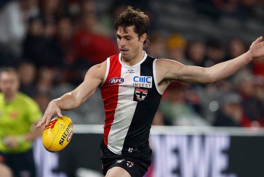 A St Kilda football player kicks a ball in front of a crowd.