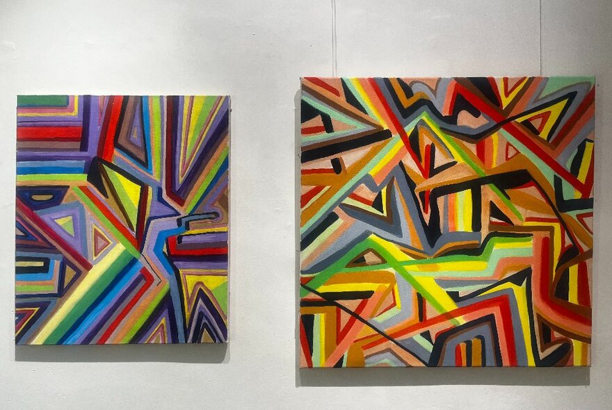 A gallery with two similar a multicoloured artworks hanging on a white wall. 