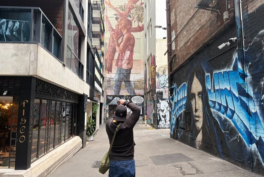 Person taking a photograph in a Melbourne graffitied laneway.