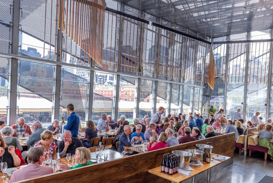 People seated in a restaurant during the day with wall-to-wall windows.