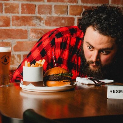 A man staring very closely at a plate with a burger and fries on, on a table with a reserved sign on it. 
