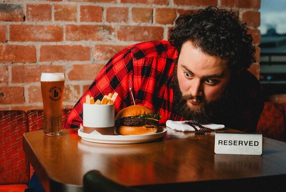 A man staring very closely at a plate with a burger and fries on, on a table with a reserved sign on it. 