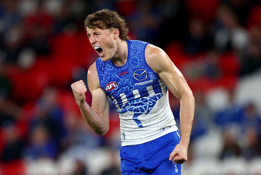 A North Melbourne AFL football player with his fists clenched and pumped during a match.