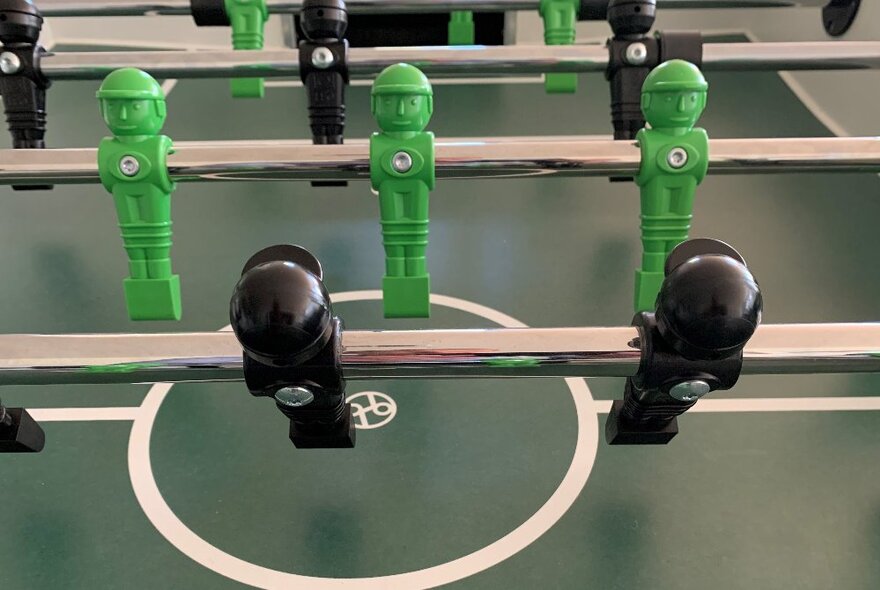 A close-up image of a foosball table with green and black players.