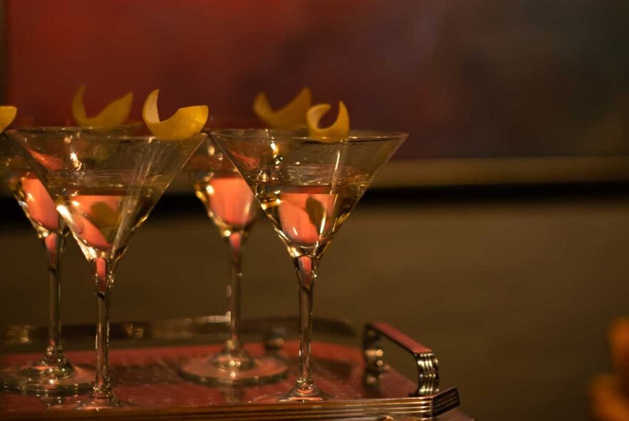 A tray in a dimly-lit room holding four martinis with a twist. 