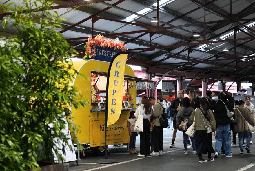 A small yellow crepe van at the Queen Victoria Market with a queue forming. 