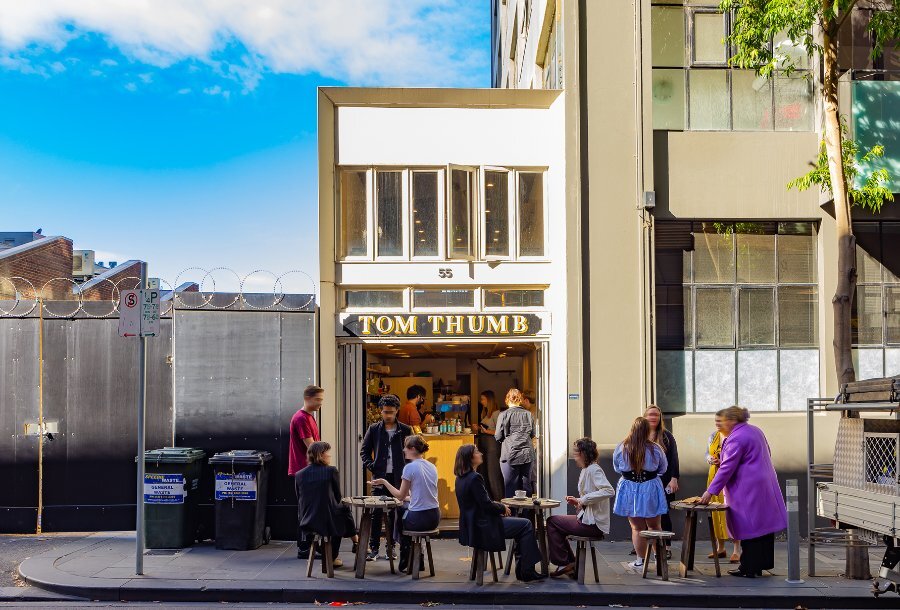 People sitting at tables outside a narrow two-story cafe. 