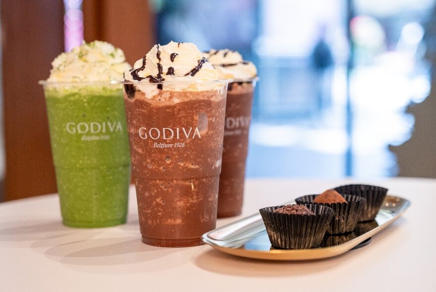 Three small chocolates and three iced drinks of matcha and chocolate varieties with whipped cream on top.