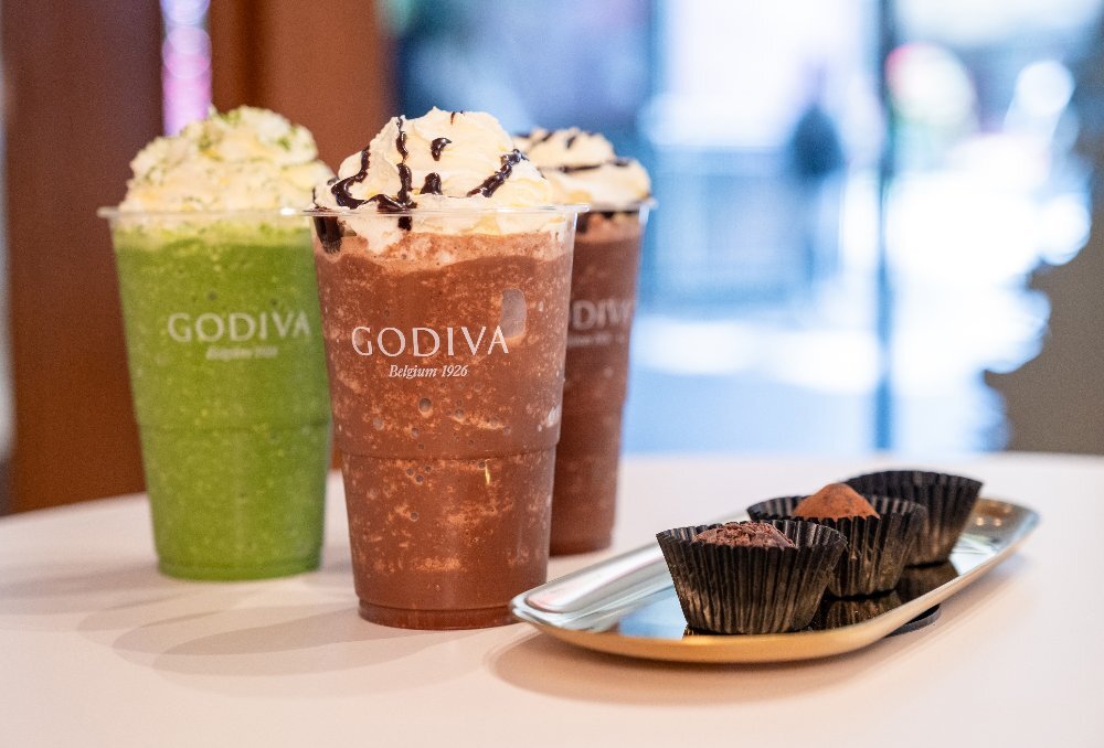 Three small chocolates and three iced drinks of matcha and chocolate varieties with whipped cream on top.