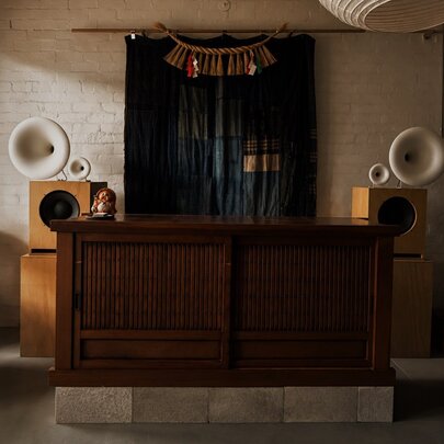 A large wooden counter inside the sparsely  furnished Nordic Japan Gallery space, with two large speakers attached to the white wall.