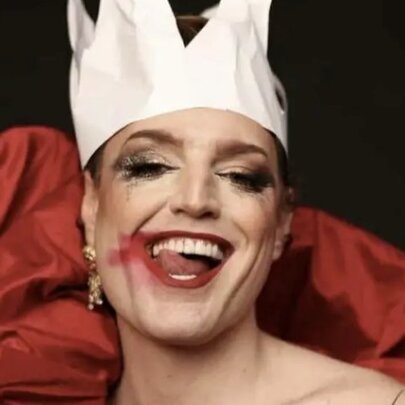Drag artist Reuben Kaye, wearing a paper crown and lipstick, licking his lips.