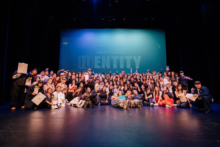 Performers gathered in a group on stage, some seated on the ground.