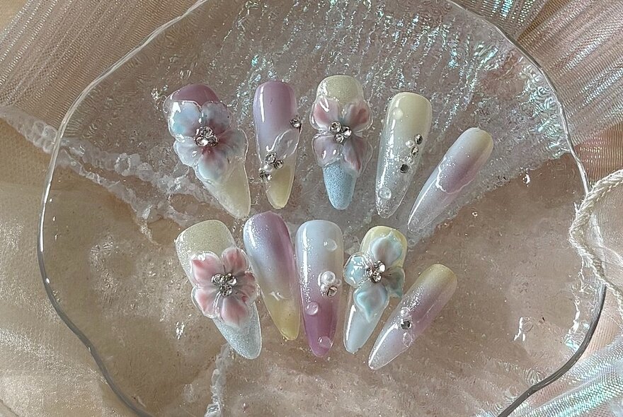 Fake fingernails decorated with flowers and studs in a glass dish.