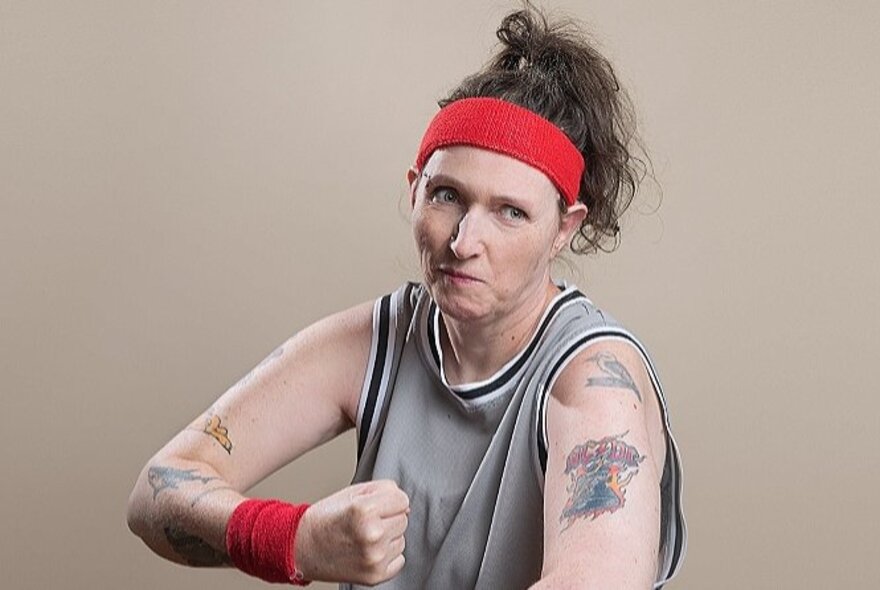 Older woman with tattooed arms making a fist, a tough expression on her face.