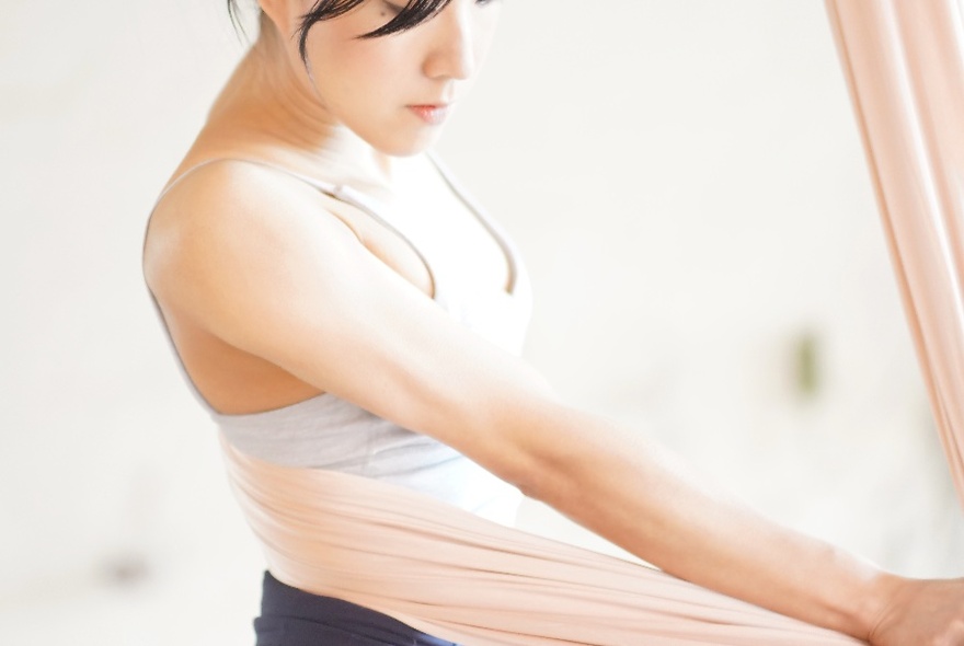Person standing in a singlet top, with the cloth of an aerial hammock wrapped around their waist.