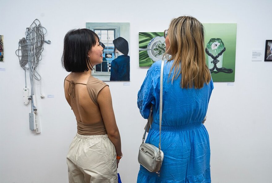 Two people standing in a gallery looking at contemporary artworks on the white walls.