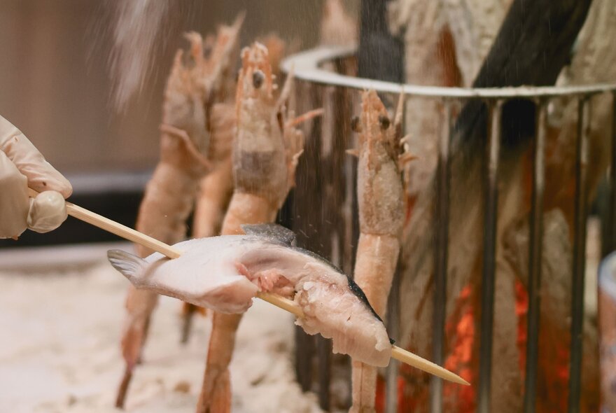 Skewered seafood grilling against wood embers in a grill.